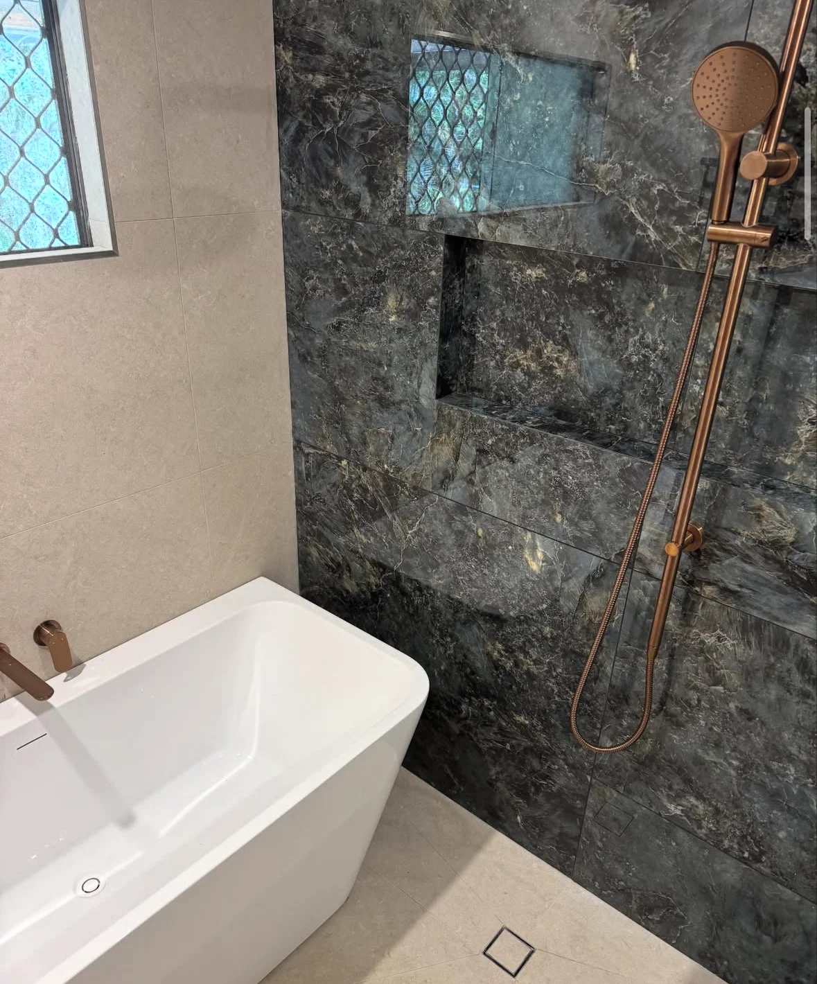 Dark stone-look bathroom tiles with copper shower fittings