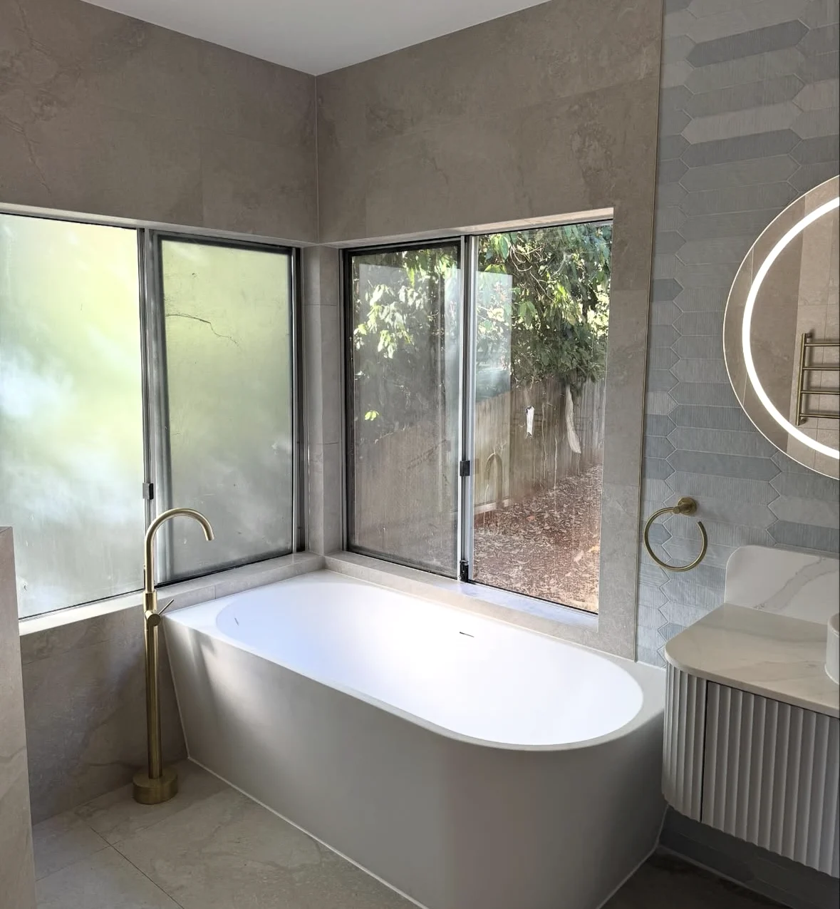 Light-filled bathroom with a freestanding bath, large grey tiles and brass fittings
